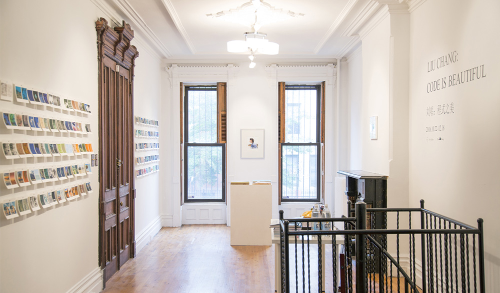 a gallery space with dozens of postcards hanging on a wall